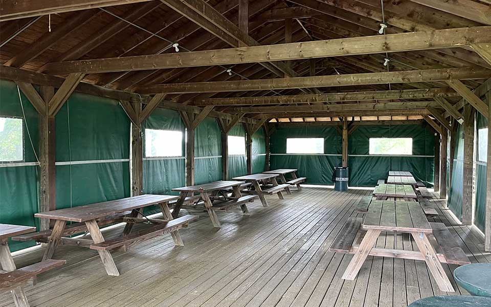 Picnic tables inside shelter with wood floor and ceiling